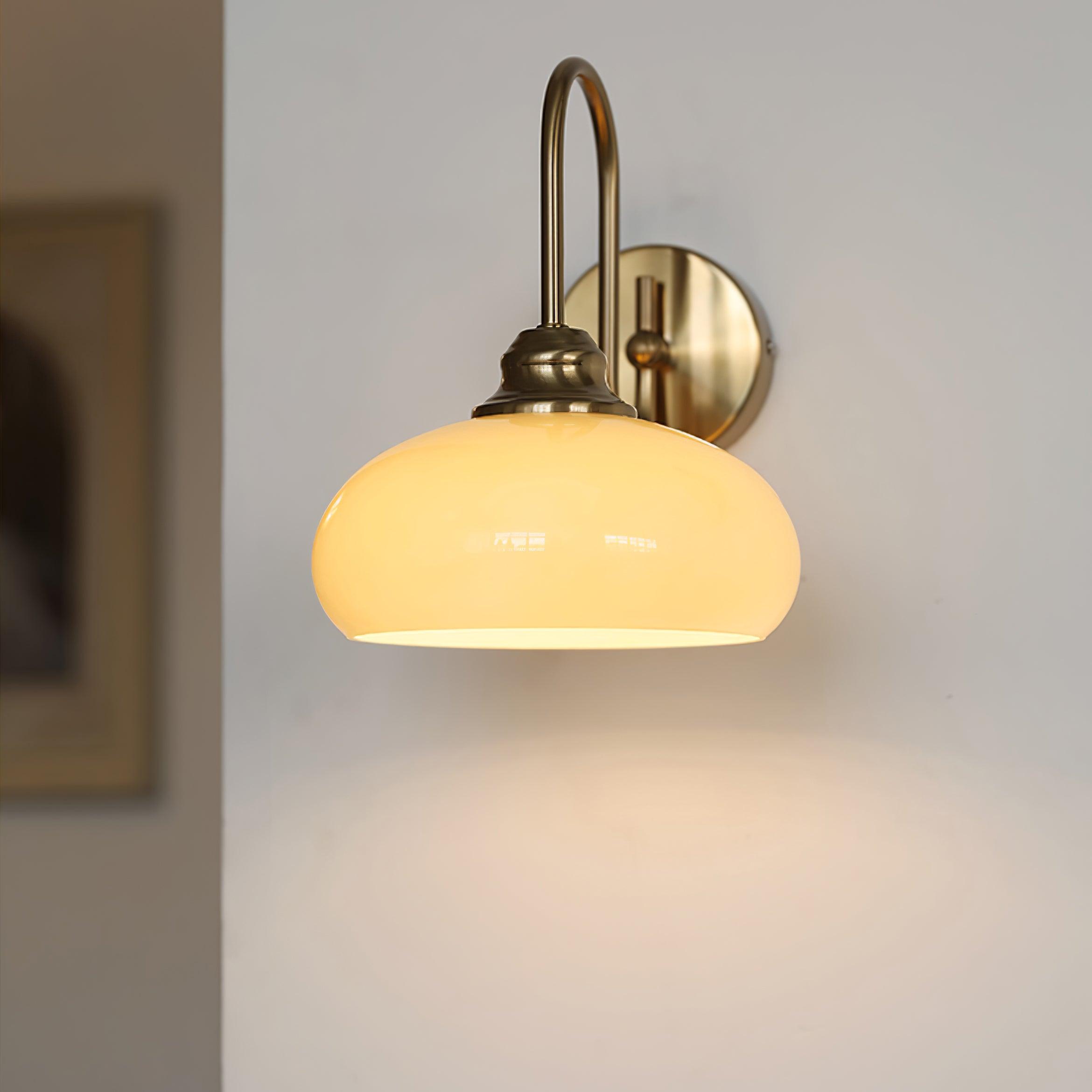 Clérachic glass wall lamp, copper arm and lit beige bowl, hardwired with a framed print blurred at left.