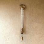 Clérachic wall light in aged gold with a fluted clear glass tube, round backplate and drop weight, shown unlit on limewash.