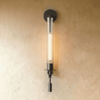 Clérachic wall light in matte black with a slim fluted clear glass tube and a tall filament bulb glowing on limewash.