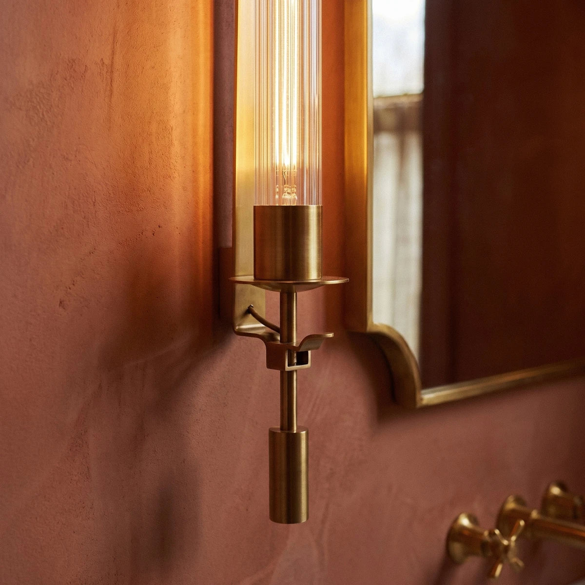 Close view of a Clérachic gold wall light, showing the brass collar, small drip tray, drop weight and fluted glass tube.