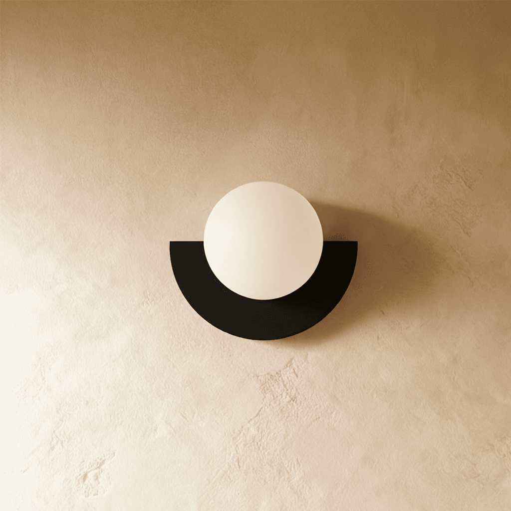 Clérachic opal glass globe on a black half-moon metal back plate, switched off, on a warm limewash plaster wall.