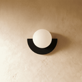 Clérachic opal glass globe on a black half-moon metal back plate, switched off, on a warm limewash plaster wall.