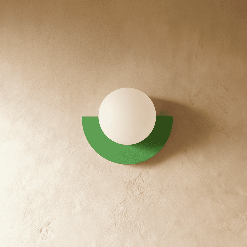 Clérachic opal glass globe on a green half-moon metal back plate, switched off, on a warm limewash plaster wall.