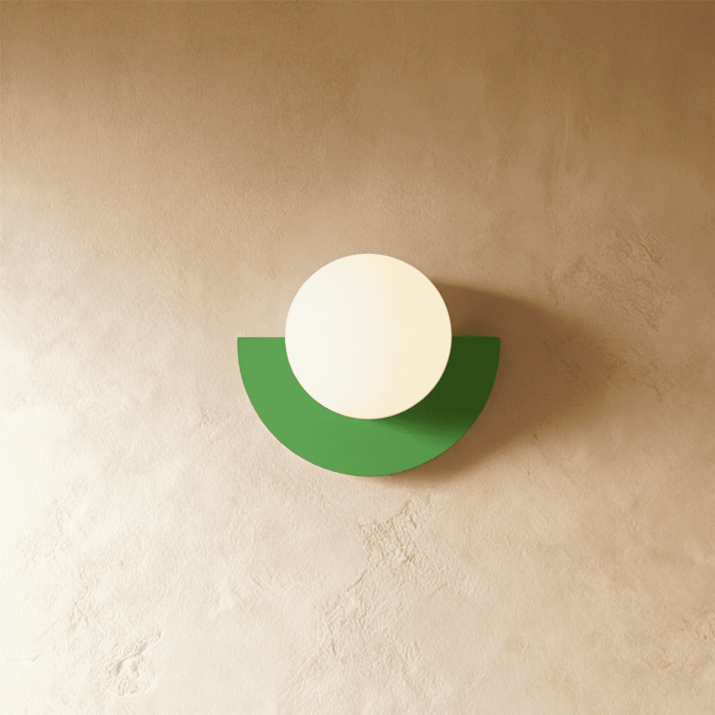 Clérachic lit opal glass globe on a green half-moon metal back plate, glowing gently on a limewash plaster wall.