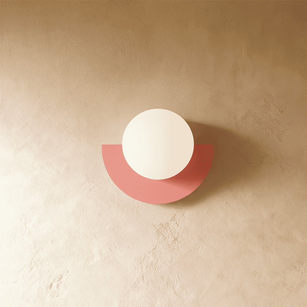 Clérachic opal glass globe on a coral-pink half-moon metal back plate, switched off, on a limewash plaster wall.
