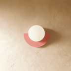 Clérachic opal glass globe on a coral-pink half-moon metal back plate, switched off, on a limewash plaster wall.