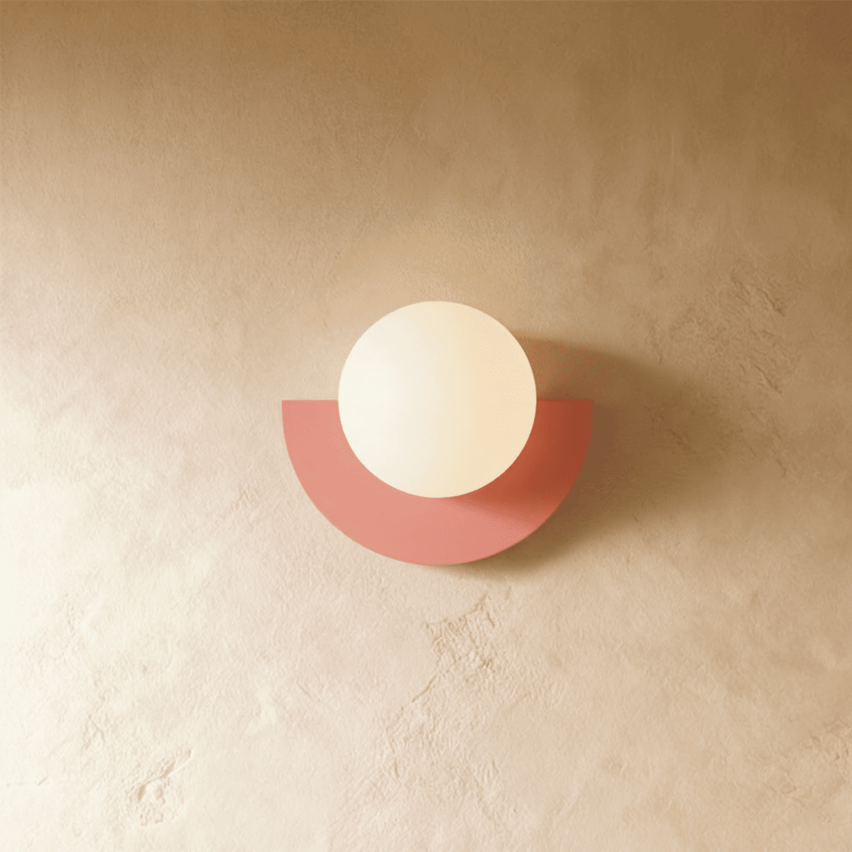 Clérachic lit opal glass globe on a coral-pink half-moon metal back plate, glowing softly on limewash plaster.