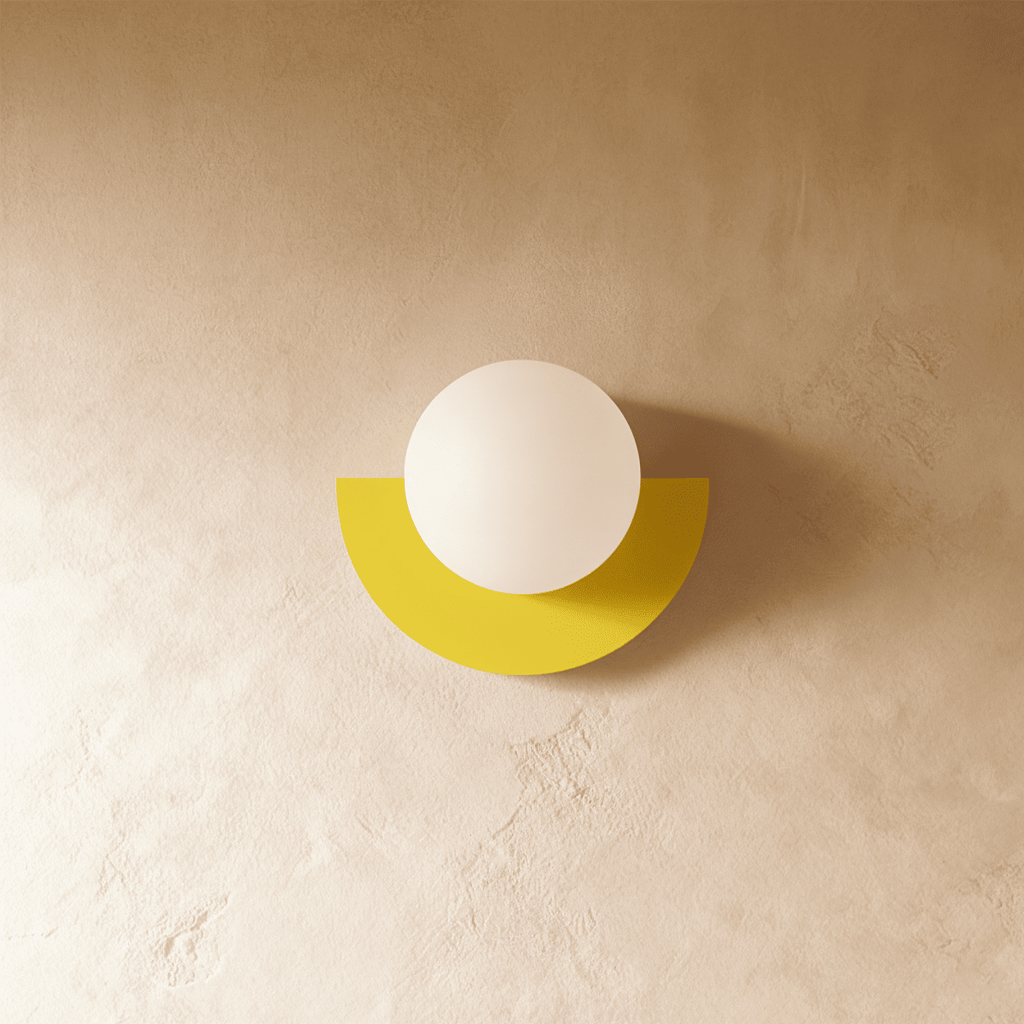 Clérachic lit opal glass globe on a yellow half-moon metal back plate, glowing softly on a limewash plaster wall.