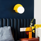 Clérachic opal glass globe wall lamp with a yellow metal back plate above a navy padded headboard and a bedside table.