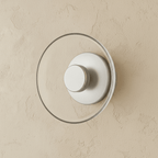 Clérachic glass uplight wall bowl in Transparent, a clear glass dome over a white centre knob, unlit on plaster.