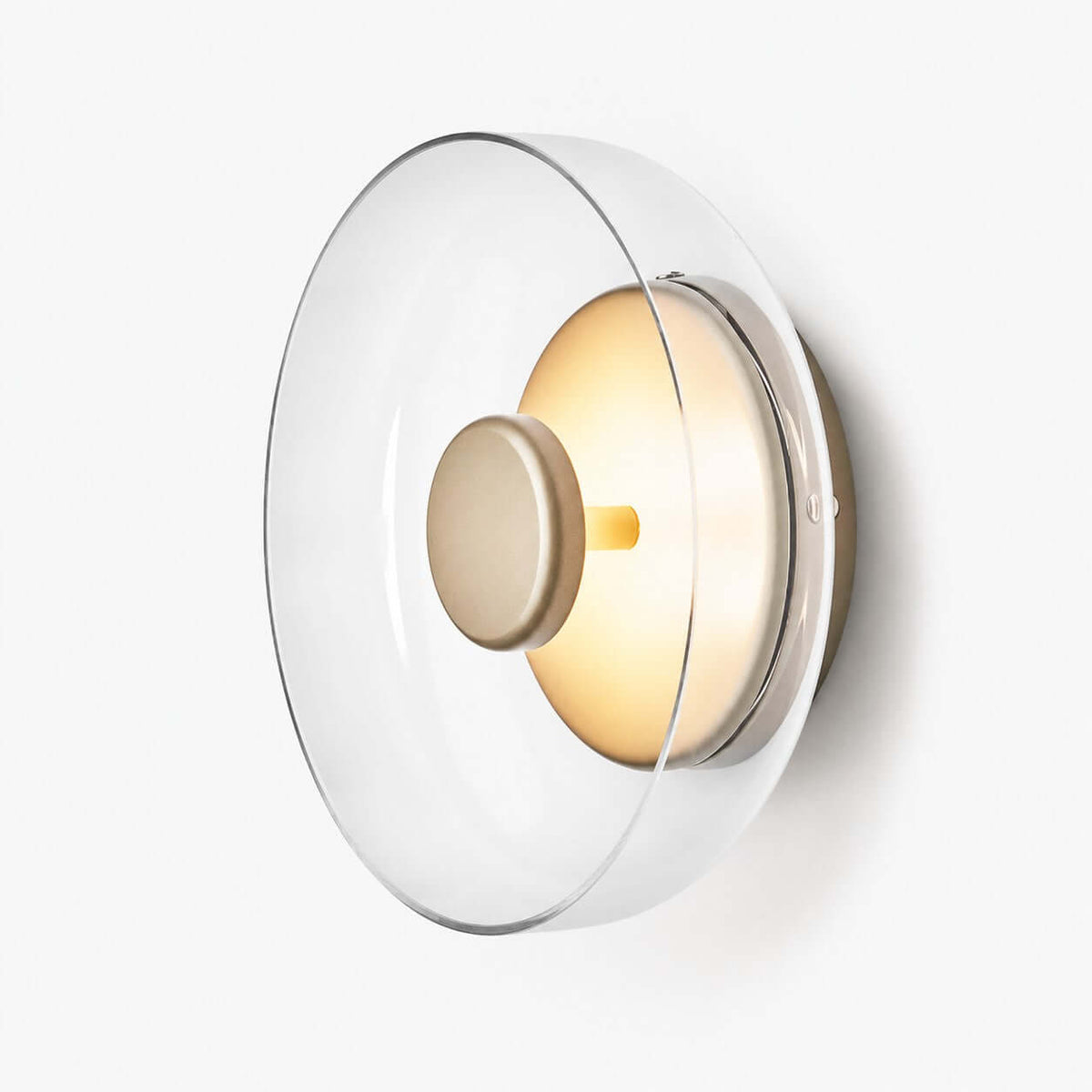 Clérachic wall light on a white backdrop, a wide clear glass disc over a gold metal backplate with a round centre cap.