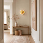 Small Clérachic wall light lit in a hallway above a wooden console, with a rug runner, a basket and a pink-toned painting.