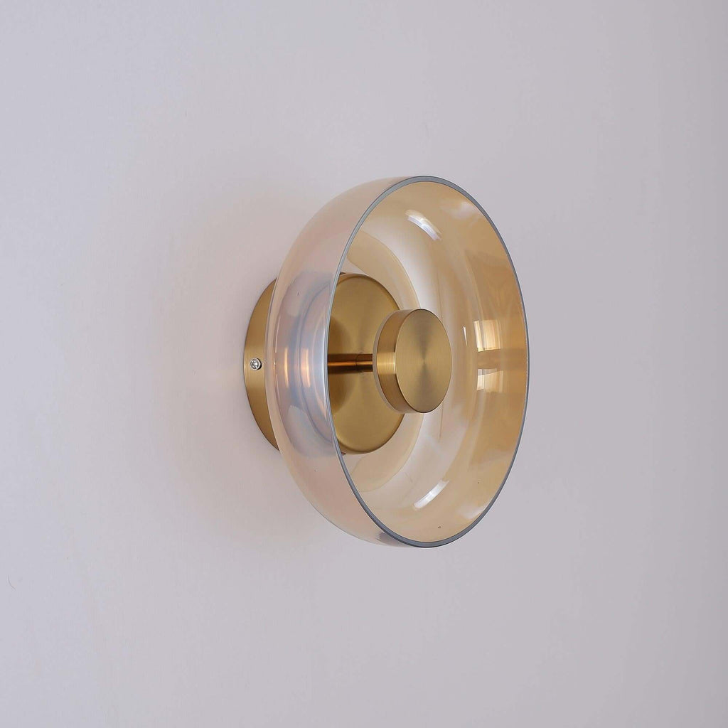 Side-on view of this Clérachic wall light in gold and amber, the glass disc standing off a round gold backplate.