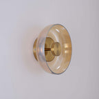 Side-on view of this Clérachic wall light in gold and amber, the glass disc standing off a round gold backplate.