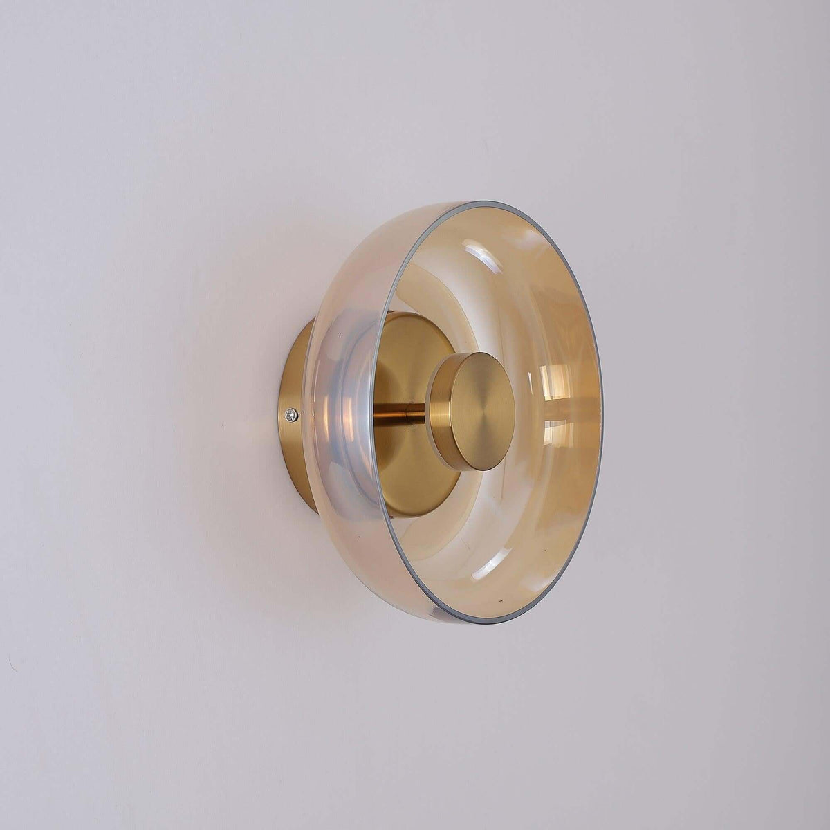 Side-on view of this Clérachic wall light in gold and amber, the glass disc standing off a round gold backplate.