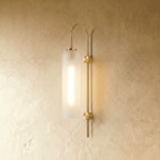 Clérachic wall light with a tall frosted glass cylinder on an arched brass arm, glowing softly against a limewashed wall.