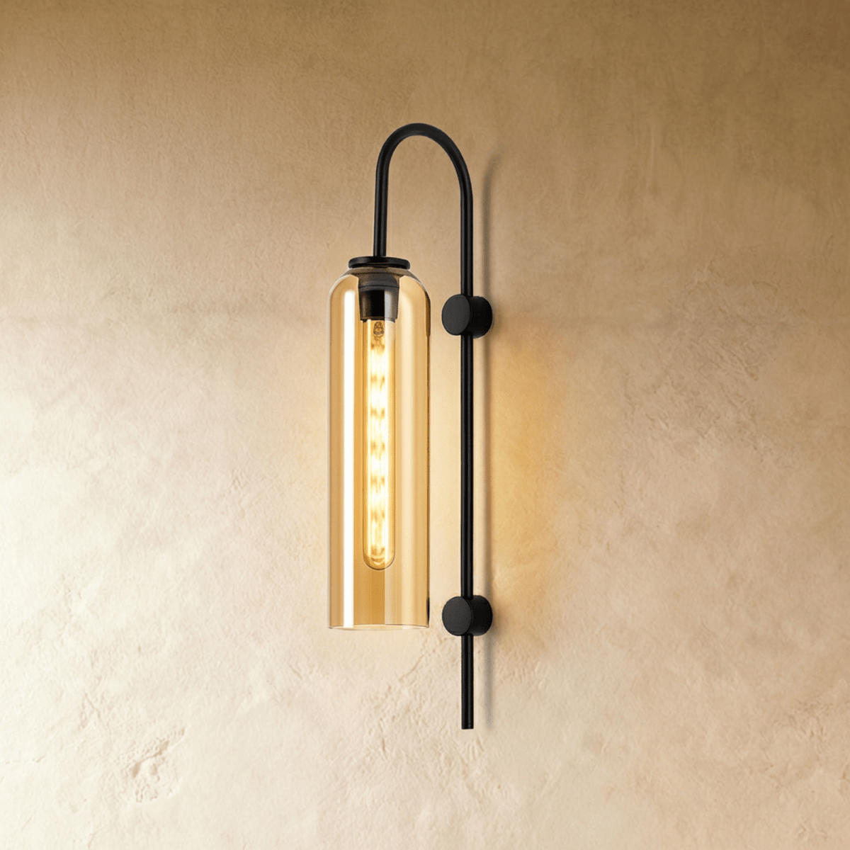Clérachic wall light with a tall amber glass cylinder on an arched black arm, a filament bulb lit against a warm plaster wall.