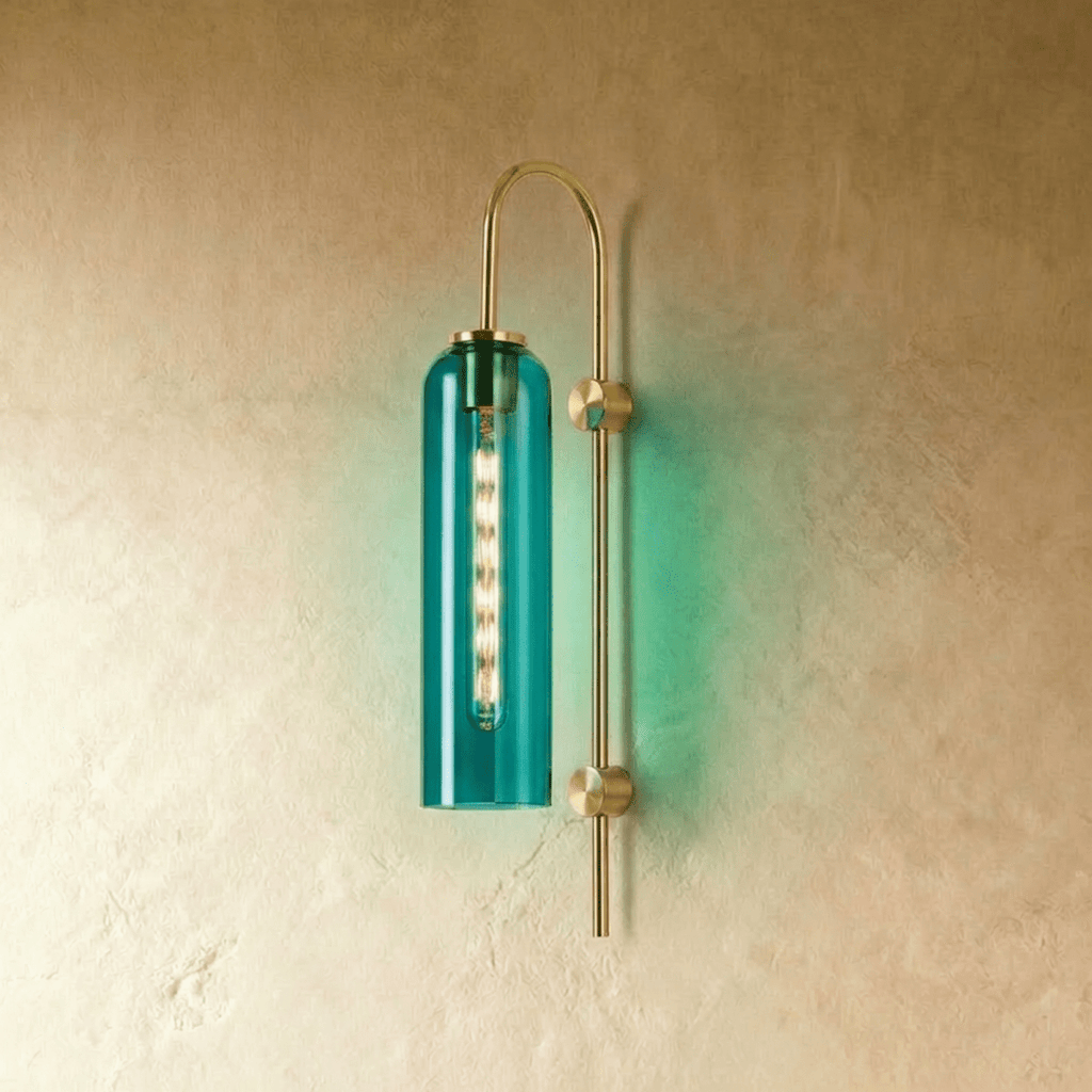 Clérachic wall light with a deep green-teal glass cylinder on an arched brass arm, casting a green glow on the wall.