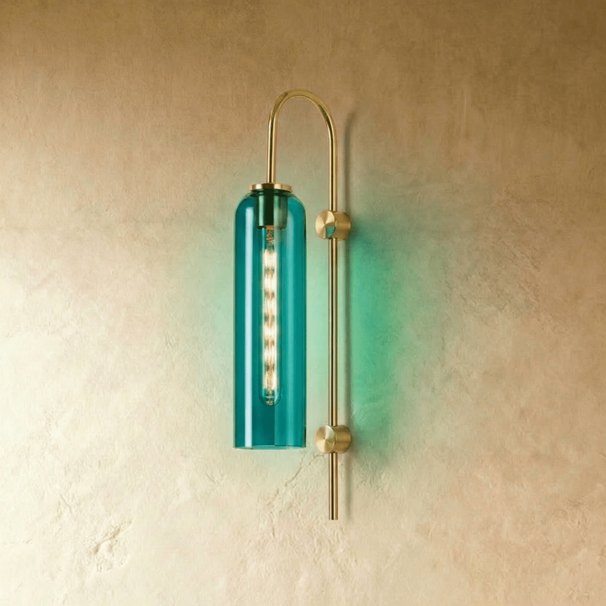 Clérachic wall light with a deep green-teal glass cylinder on an arched brass arm, casting a green glow on the wall.