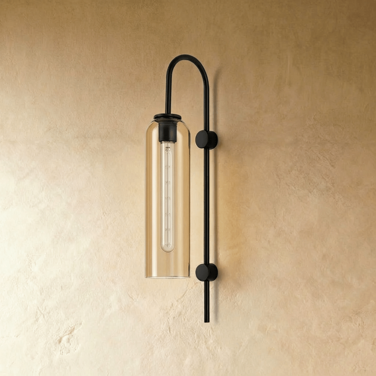 Clérachic wall light with an amber glass cylinder and clear tube bulb, unlit, on an arched matte black arm and plaster wall.