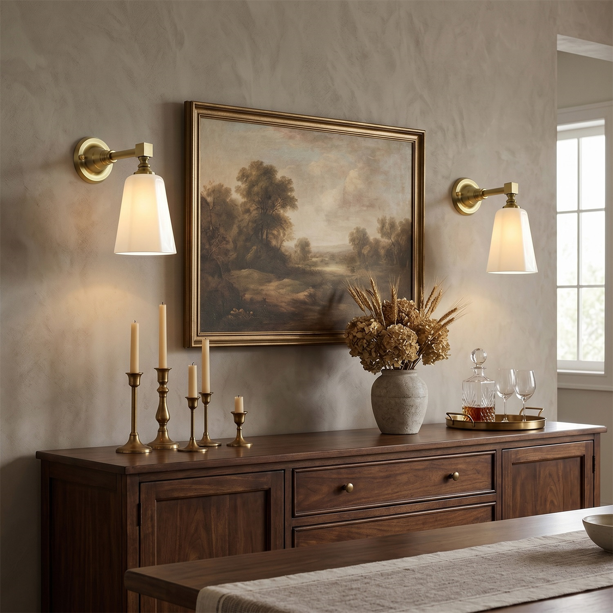 Two gold Clérachic wall sconces with white shades flank a framed landscape painting above a dark wood sideboard with candlesticks.