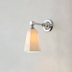 Chrome Clérachic wall sconce lit, its tapered white glass shade glowing warm beneath a polished arm and round chrome backplate.