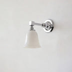 Chrome Clérachic wall light with a smaller flared bell-shaped white glass shade, switched off, on a pale grey wall.