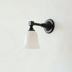 Black Clérachic wall light with a flared bell-shaped white glass shade, switched off, mounted on a pale grey wall.