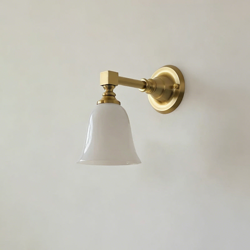 Gold Clérachic wall light with a flared bell-shaped white glass shade, switched off, on a pale grey wall.
