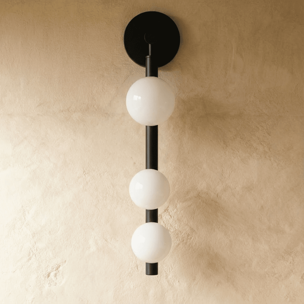 Clérachic black wall lamp with three opal glass spheres on a vertical rod, unlit, against a limewash wall.