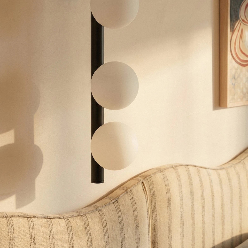 Clérachic black wall lamp detail, three frosted glass spheres on a slim black rod above a striped upholstered headboard.