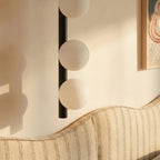 Clérachic black wall lamp detail, three frosted glass spheres on a slim black rod above a striped upholstered headboard.
