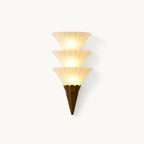 Clérachic wall sconce with three stacked ribbed white glass cones above a brown pointed base, lit, on a plain white backdrop.