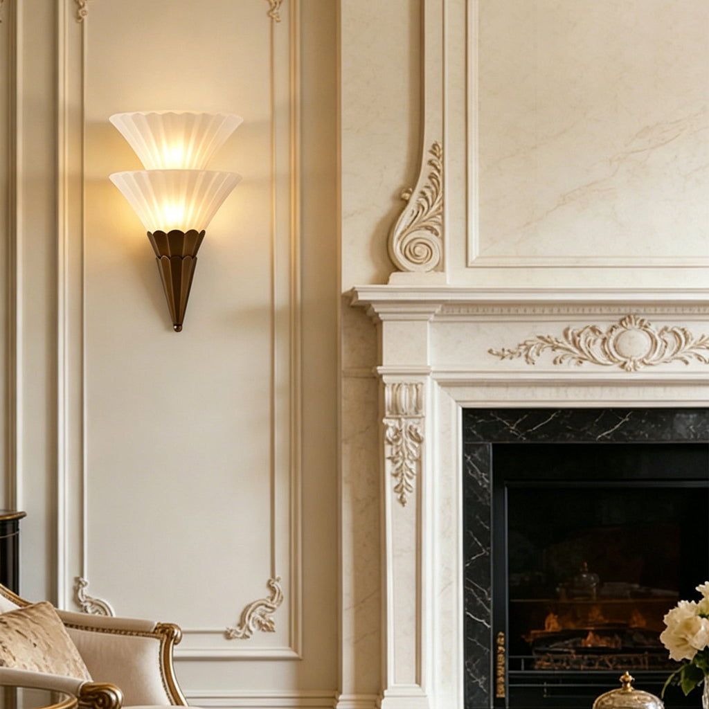 Two-cone Clérachic wall sconce lit beside a carved white fireplace with a marble surround and a lit fire.