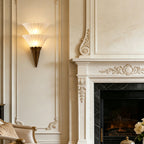 Two-cone Clérachic wall sconce lit beside a carved white fireplace with a marble surround and a lit fire.
