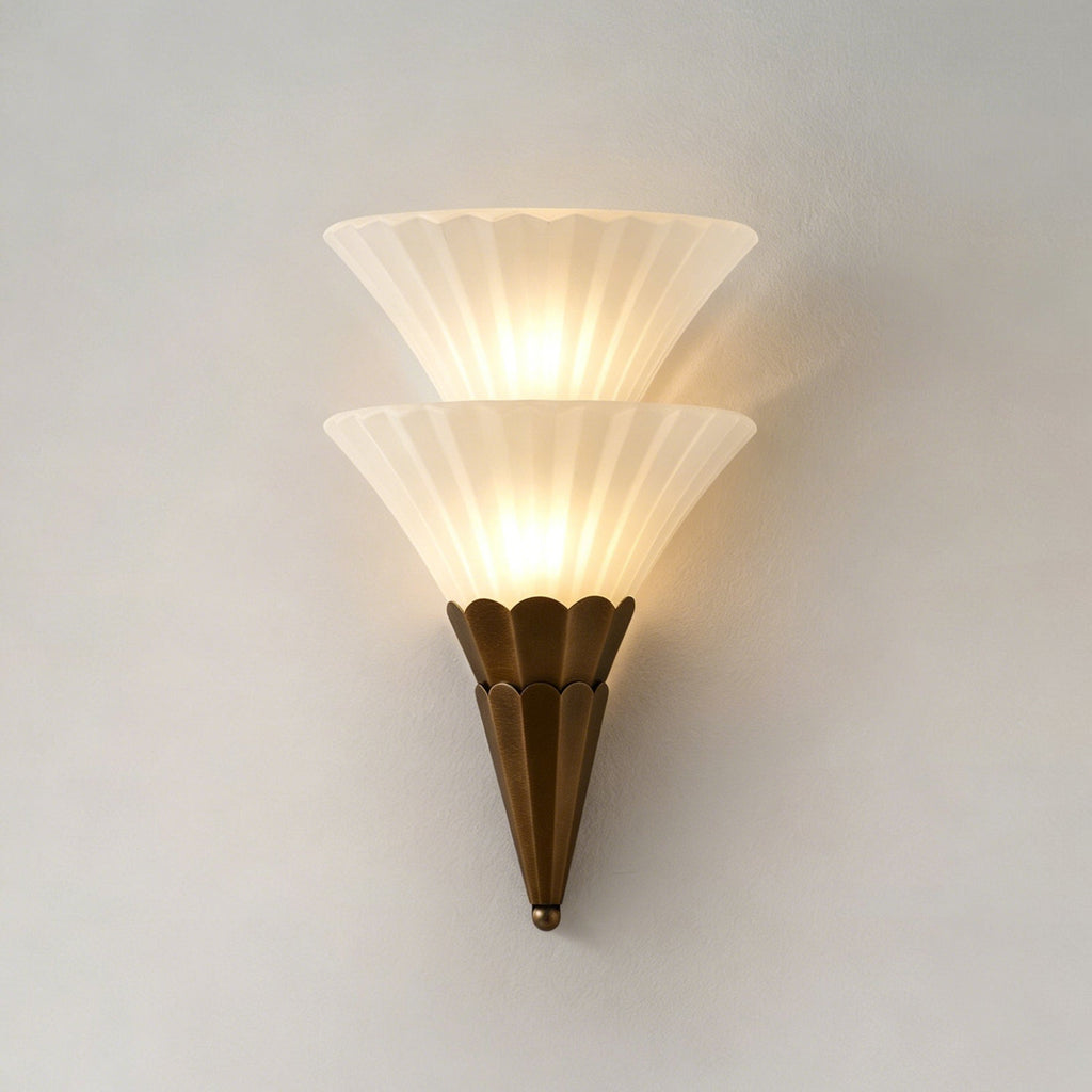 Two stacked ribbed glass cones on a brown scalloped base, lit warm on a pale wall, on this Clérachic wall sconce.