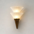 Two stacked ribbed glass cones on a brown scalloped base, lit warm on a pale wall, on this Clérachic wall sconce.