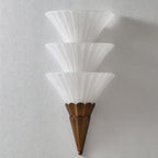 Unlit Clérachic wall sconce with three stacked frosted glass cones and a brown tapered base on a grey wall.