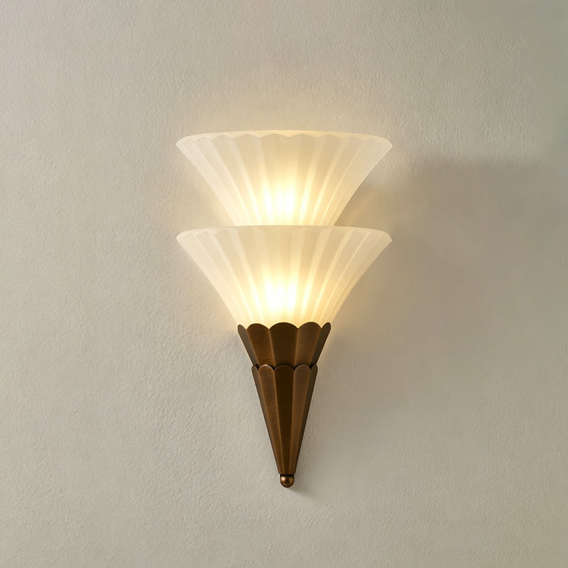 Two-cone Clérachic wall sconce lit warm on a pale grey wall, with a soft shadow falling to the right.
