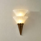 Two-cone Clérachic wall sconce lit warm on a pale grey wall, with a soft shadow falling to the right.