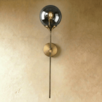 Clérachic wall sconce in antique brass with a smoked gray glass globe shade lit warm white on a straight stem.