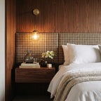 Clérachic wall sconce in brass with a clear glass globe shade lit warm white above a walnut nightstand and plaid headboard.