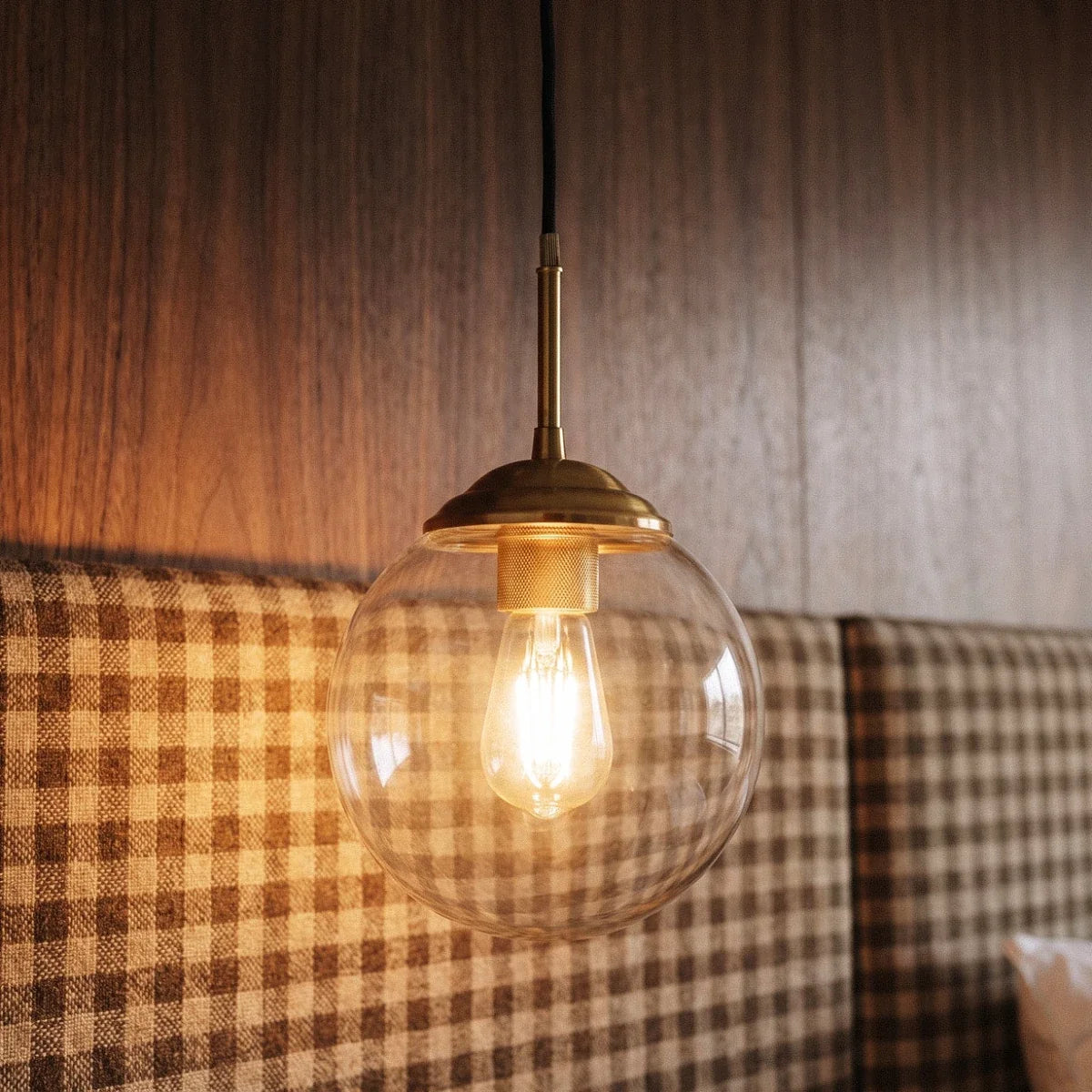 Clérachic wall sconce in brass with a clear glass globe shade lit warm white, close view of the drop arm and fabric cord.