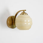 Studio shot of the Clérachic lantern wall sconce in gold with a beige glass shade and circular backplate.