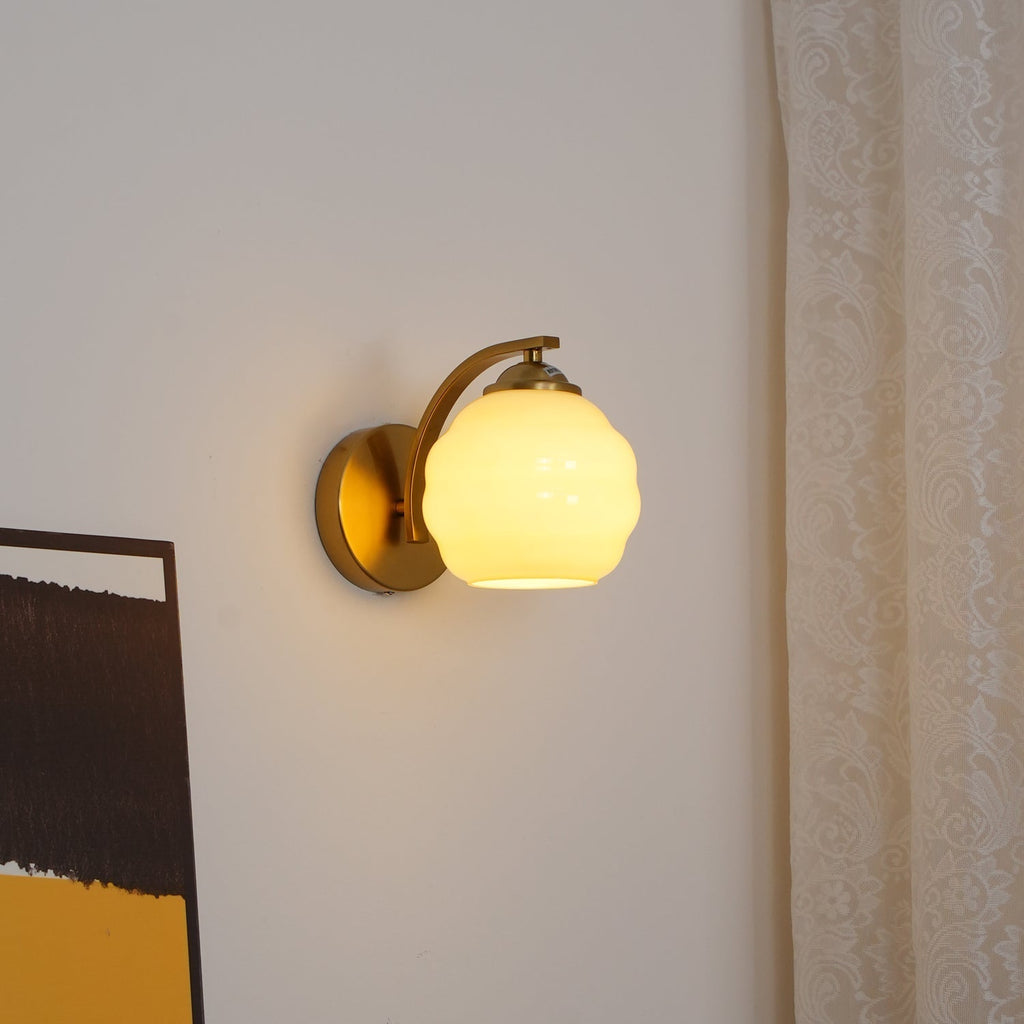 Lit Clérachic gold wall sconce with a warm beige lantern shade beside a patterned white curtain.
