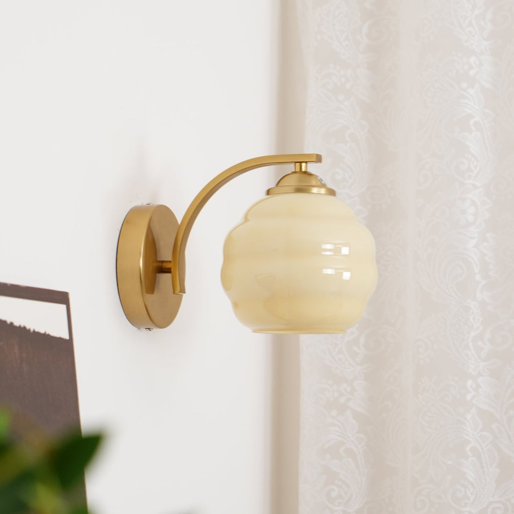 Clérachic gold wall sconce with a beige lantern shade beside a lace curtain, a picture and foliage below.