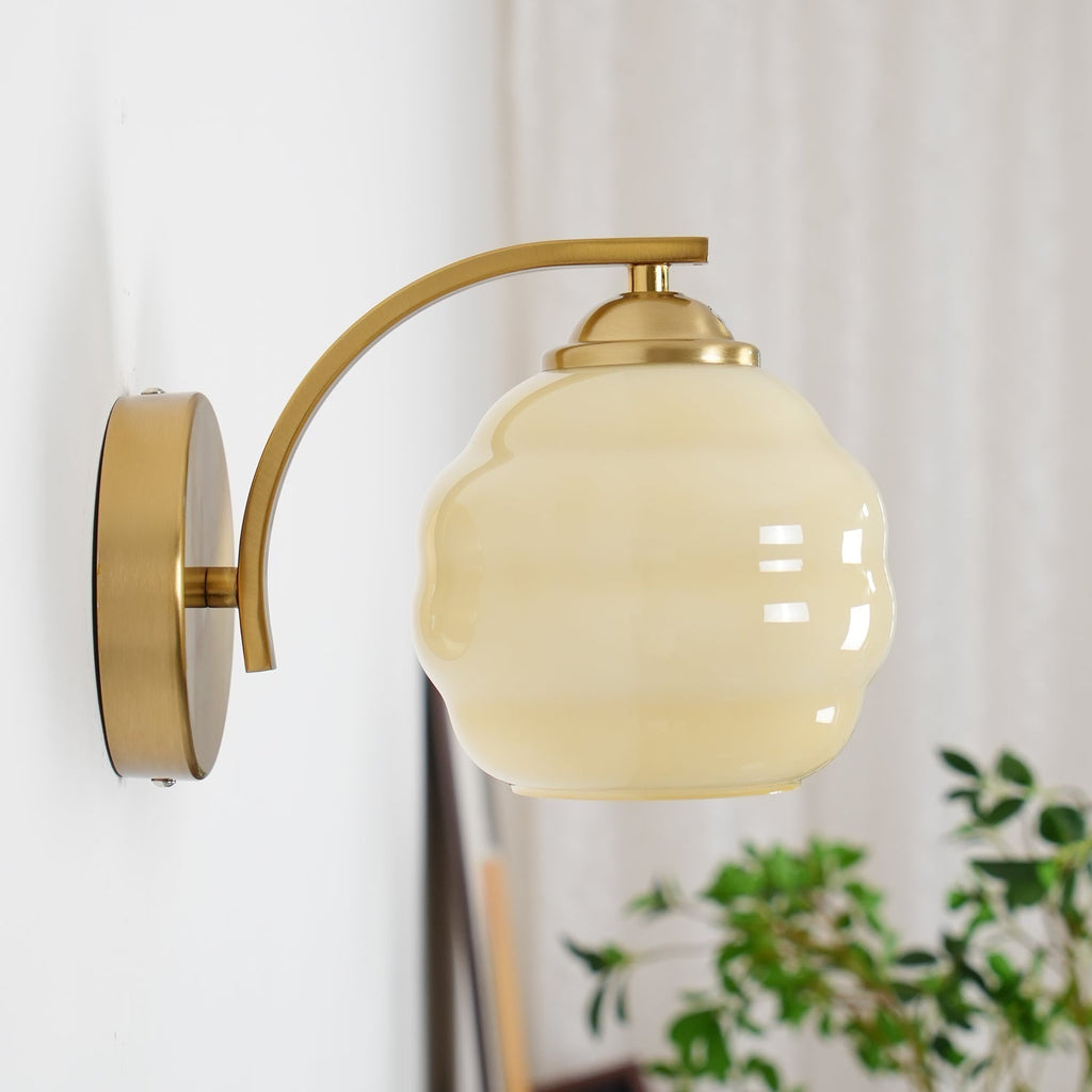 High-angle view of the Clérachic gold wall sconce and beige lantern shade, a plant and curtain behind.
