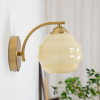 High-angle view of the Clérachic gold wall sconce and beige lantern shade, a plant and curtain behind.