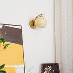 Unlit Clérachic gold wall sconce with a beige lantern shade beside abstract art, a floral print and a curtain.