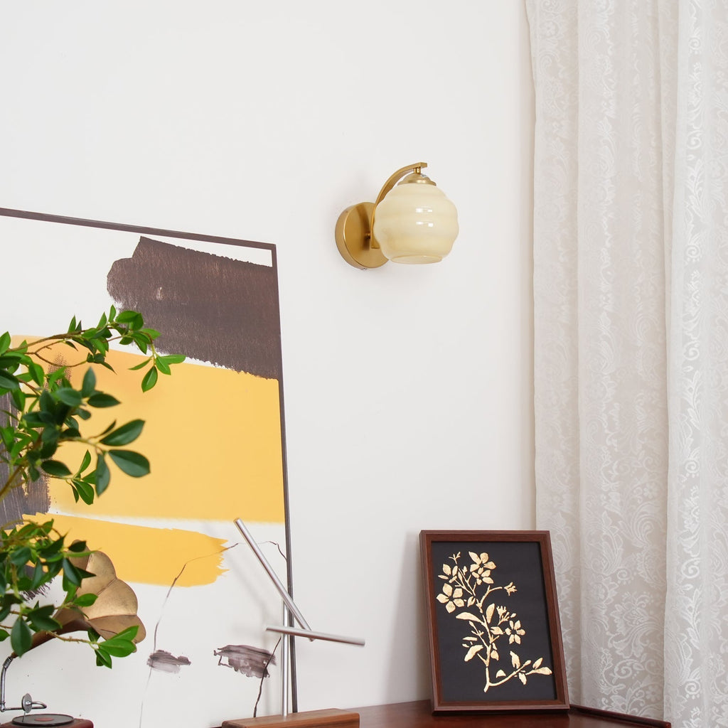 Clérachic gold wall sconce with a beige lantern shade in a living room, abstract painting and lace curtain nearby.